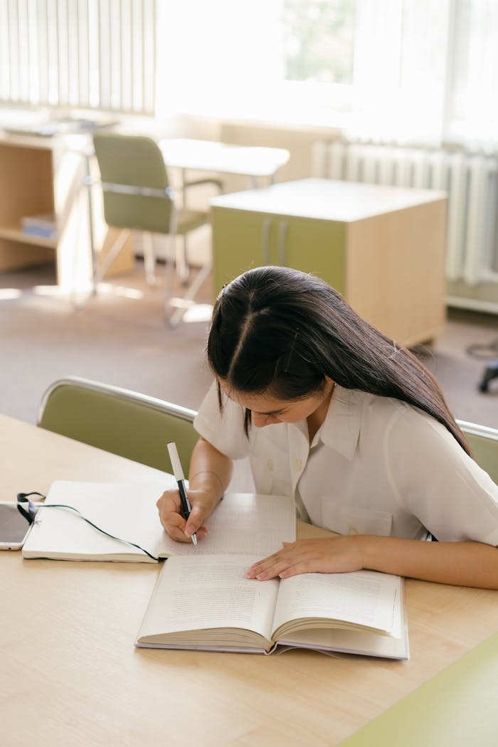 Young woman writing in a notebook, studying at a library table.